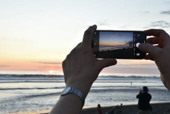Hands holding a smartphone taking a photo of a beach sunset - mastering exposure on your phone